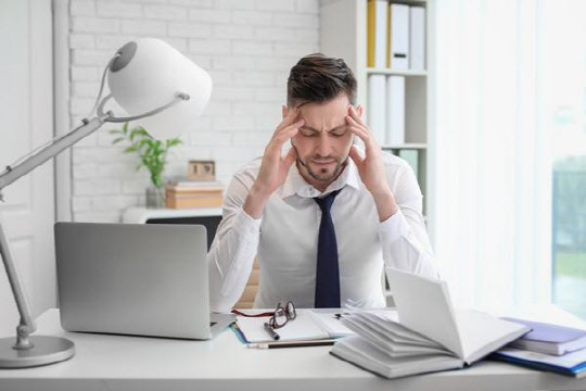 Man suffering from headache while sitting at table in office